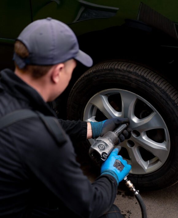 Auto mechanic in a cap changing a wheel from a black car using a drill in a tire shop on the street detailing car repairs Auto mechanic in a cap changing a wheel from a black car using a drill in tire shop on the street detailing car repairs