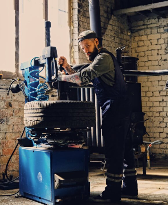 Bearded mechanic changing car's tire on a tire. Bearded mechanic changing car's tire on a tire changing machine in a workshop.